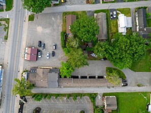 An aerial view of a parking lot with several cars, a building with a red roof, and surrounding greenery.