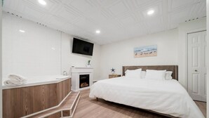 Ein Schlafzimmer mit einem großen Bett, einem Kamin, einem Fernseher und einem Badezimmer mit Waschbecken und Spiegel.