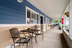 A covered outdoor area with a table and chairs, a window, and a hanging flower pot.