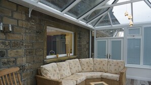 A conservatory with a curved wicker sofa, a wooden chair, and a glass table.