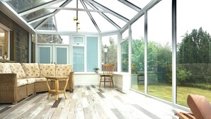 A conservatory with a curved sofa, a wooden chair, and a small table.