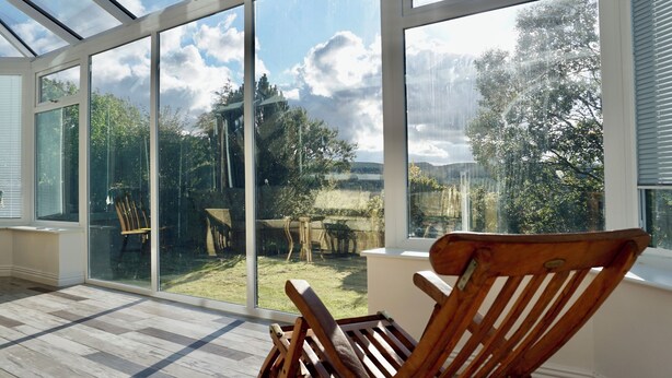 A conservatory with large glass doors, a wooden chair, and a view of a garden.