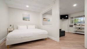 A bedroom with a bed, a nightstand, a TV, and a kitchenette. - King Jacuzzi Suite | The Beachside Co. #9 (Sylvan Beach)