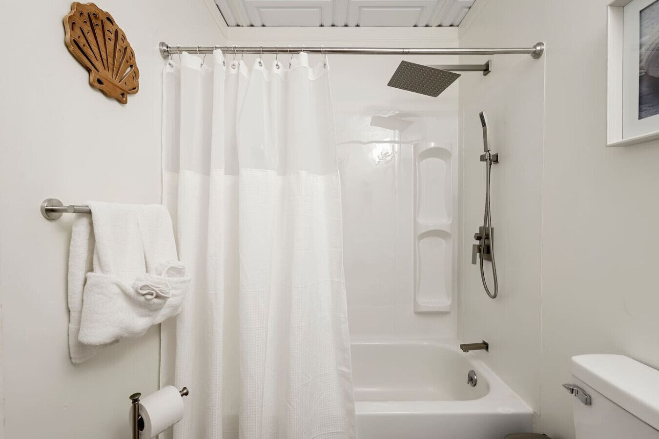 Un baño con ducha, bañera, inodoro, toallero y dispensador de papel higiénico.