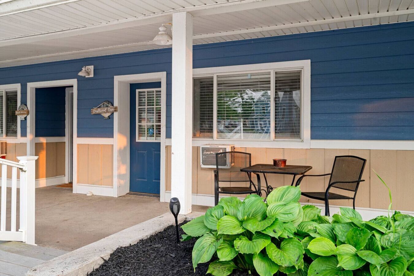 A blue building with a porch, a table, and two chairs.