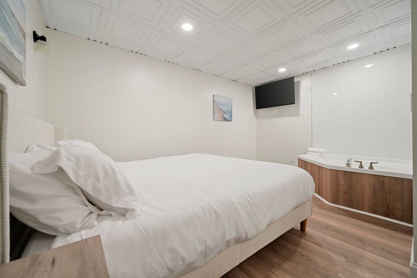 Ein Schlafzimmer mit Bett, Nachttisch, an der Wand montiertem Fernseher und einem Badezimmer mit Waschbecken und Spiegel.