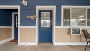 Une maison bleue avec une porte bleue, un revêtement de couleur beige et une enseigne sur laquelle on peut lire « Driftwood Den ».