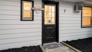 A house with a black front door, a sign above the door, and two windows with blinds. - Cozy Beach Studio | The Beachside Co. #6 (Sylvan Beach)