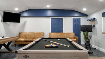 A pool table with a cue stick and balls, two leather sofas, a television mounted on the wall, and a door with a blue frame.
