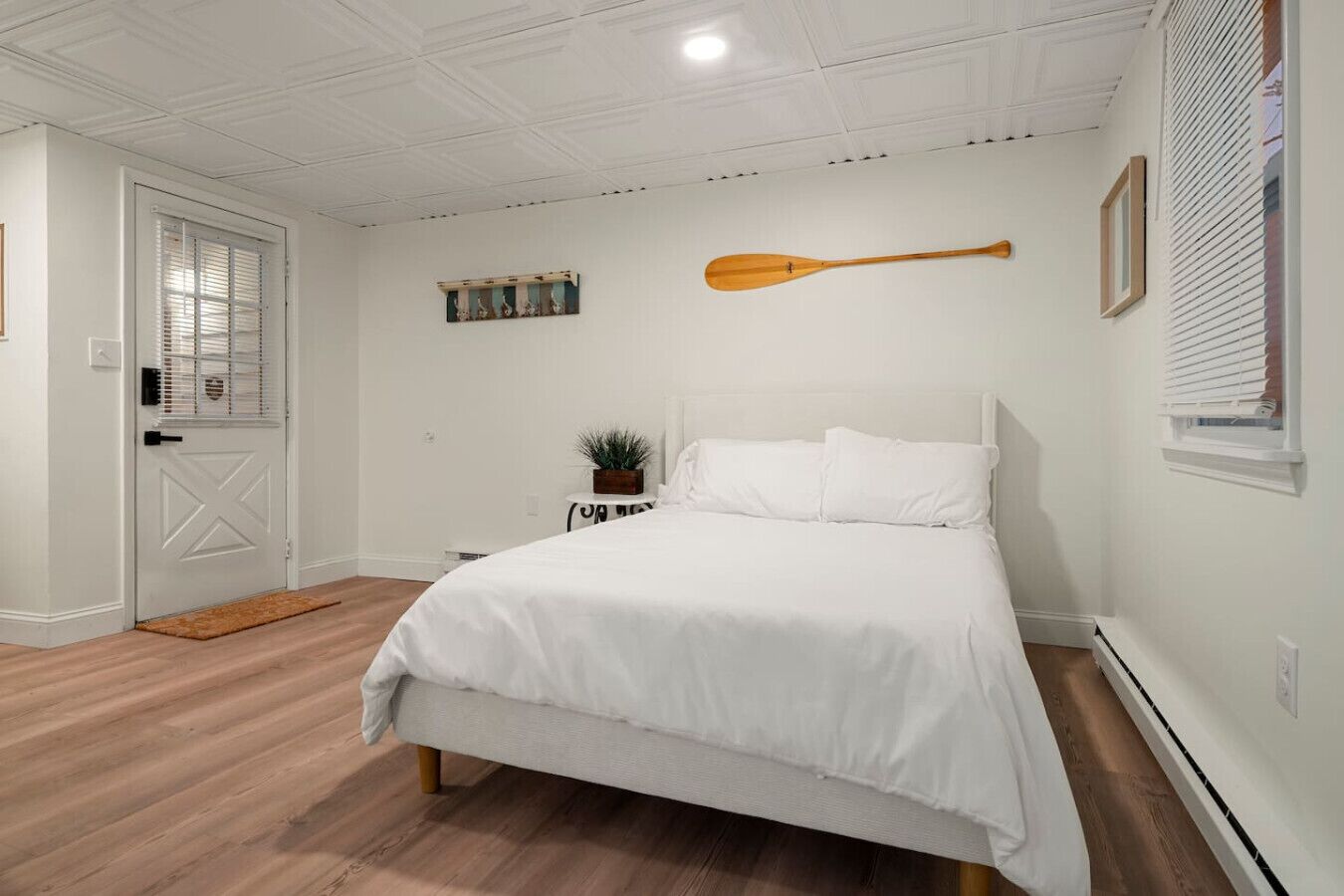 Une chambre à coucher avec un lit, une pagaie en bois, une petite table avec une plante et une porte avec une fenêtre.