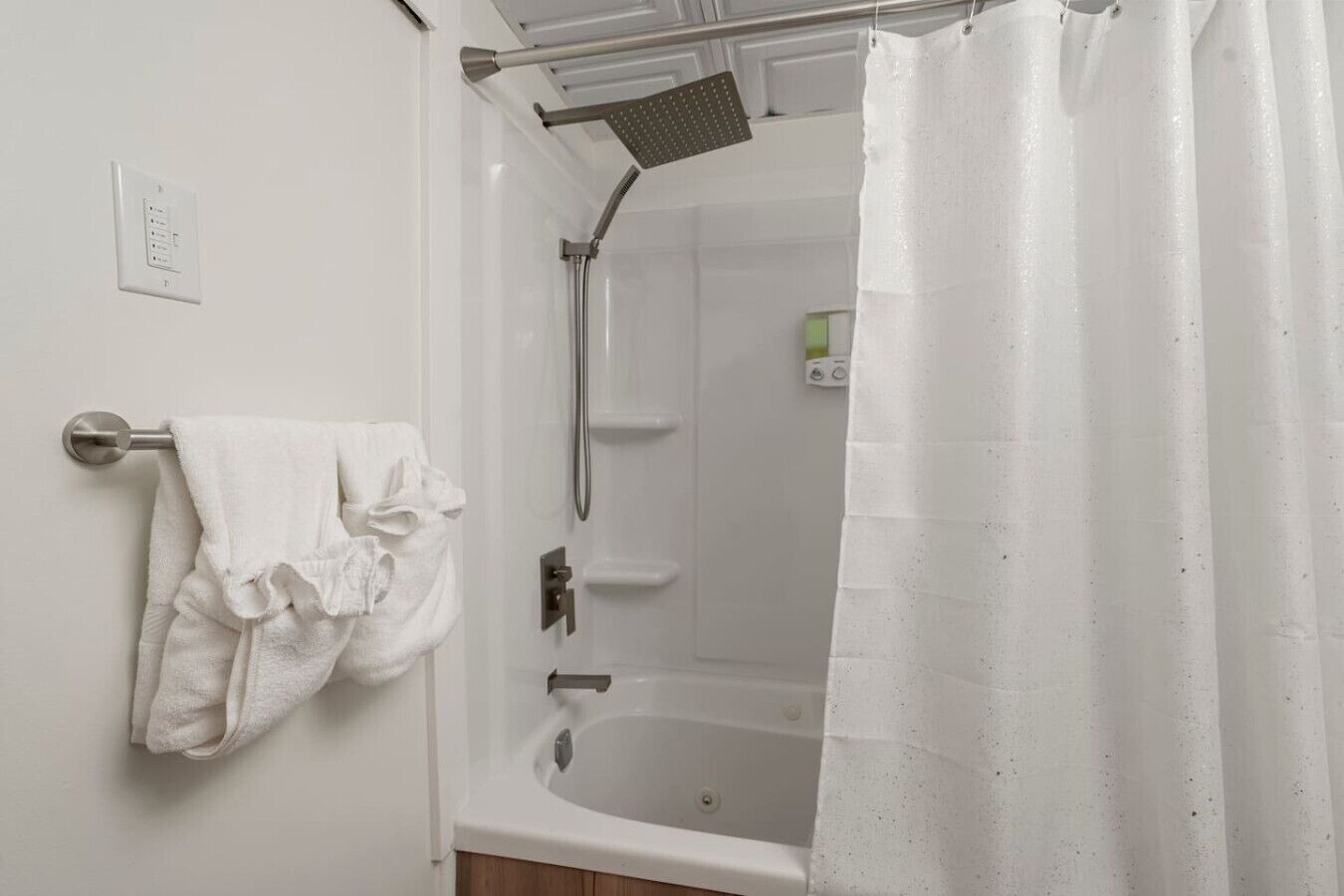A bathroom with a bathtub, a showerhead, a towel rack with a towel, and a control panel.