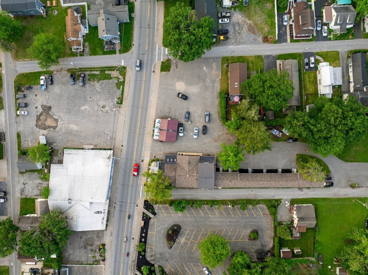 An aerial view of a residential area with houses, a main road, and a parking lot.