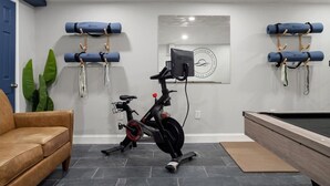 Un gimnasio en casa con equipo de ejercicio, mesa de billar y un sofá de cuero.