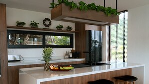 A modern kitchen with a central island, wooden bar stools, and a window with blinds. - Villa Jaisai 4-bedroom Sea View & On-Site chef (Chaweng)