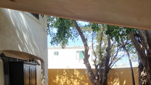 An outdoor patio with a round table and chairs, a cabinet, and trees providing shade.