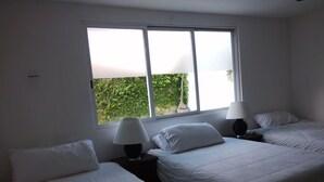 A hotel room with two beds, a window with a view of greenery, and two bedside lamps.
