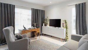 Een moderne woonkamer met een flatscreen televisie, een houten bureau en twee grijze fauteuils.