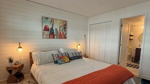 Une chambre à coucher avec un grand lit, deux lampes de chevet, un tableau accroché au mur et une porte donnant sur une salle de bain.