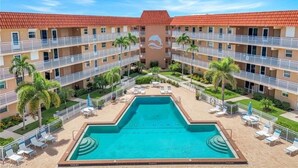 Un hôtel doté d’une piscine centrale, entourée de nombreux balcons, de palmiers et de chaises longues.