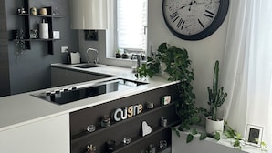 A modern kitchen with a central island, a large wall clock, and a window with blinds. - Charming and art house in the middle of Como, Milan and lugano. (Fino Mornasco)