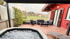 A hot tub with a view of a sports field, outdoor furniture, and a red building in the background. - Charming and art house in the middle of Como, Milan and lugano. (Fino Mornasco)