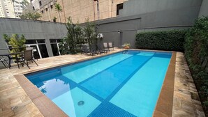 Ein rechteckiger Swimmingpool mit Fliesenrand, umgeben von Steinplatten und einigen Kübelpflanzen.