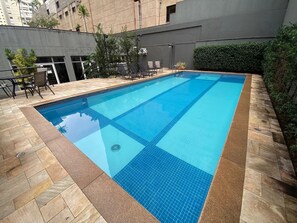Ein rechteckiger Swimmingpool mit Fliesenrand, umgeben von Steinplatten und einigen Kübelpflanzen.