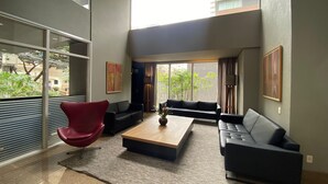 Ein modernes Wohnzimmer mit einem roten Sessel, zwei Sofas, einem Couchtisch und großen Fenstern mit Blick auf die Stadt.