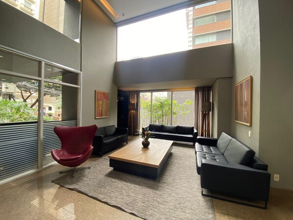 A modern living room with a red chair, two sofas, a coffee table, and large windows offering a view of the city.