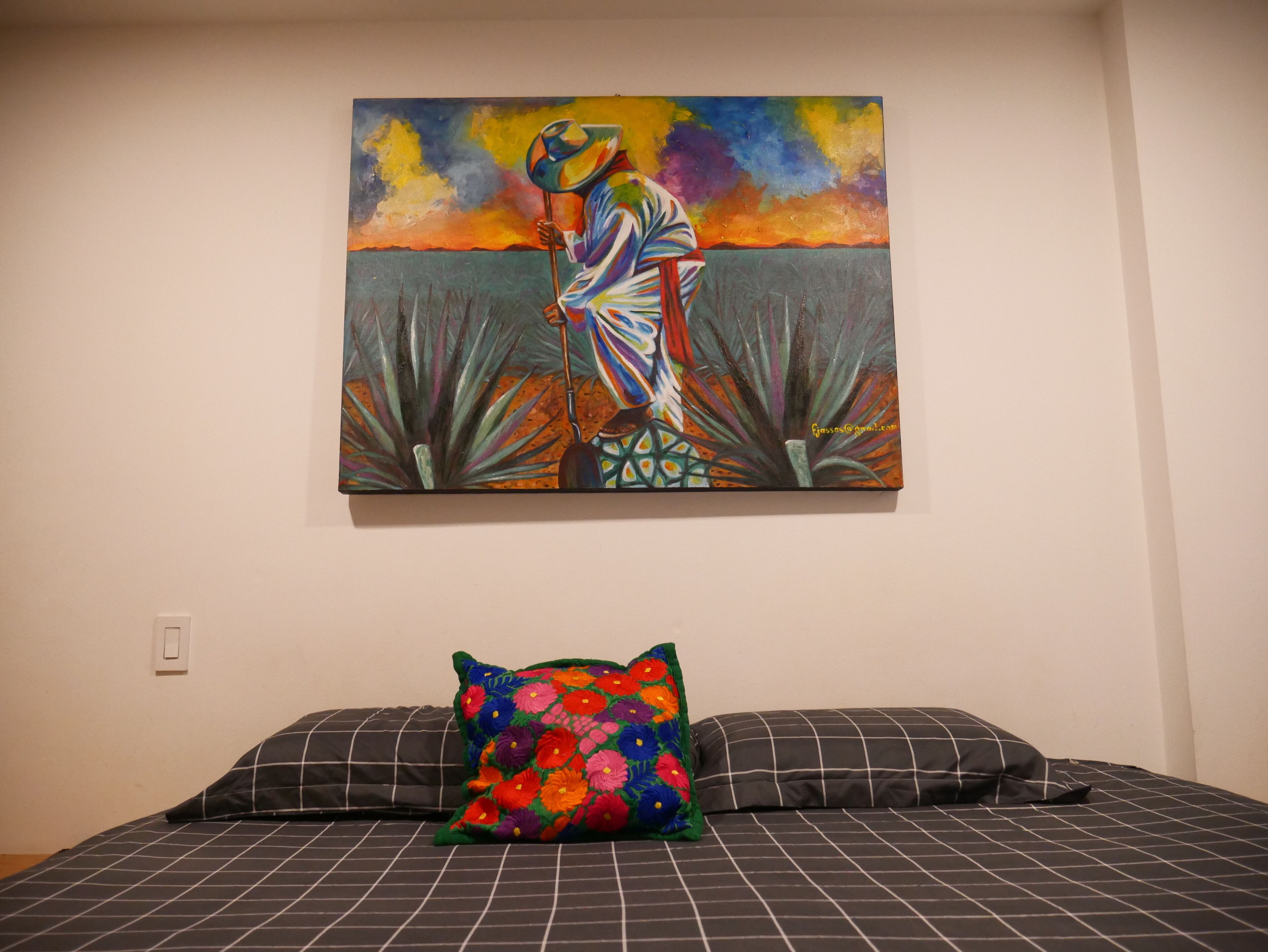 Une chambre à coucher avec un lit, deux oreillers et un tableau coloré accroché au mur.