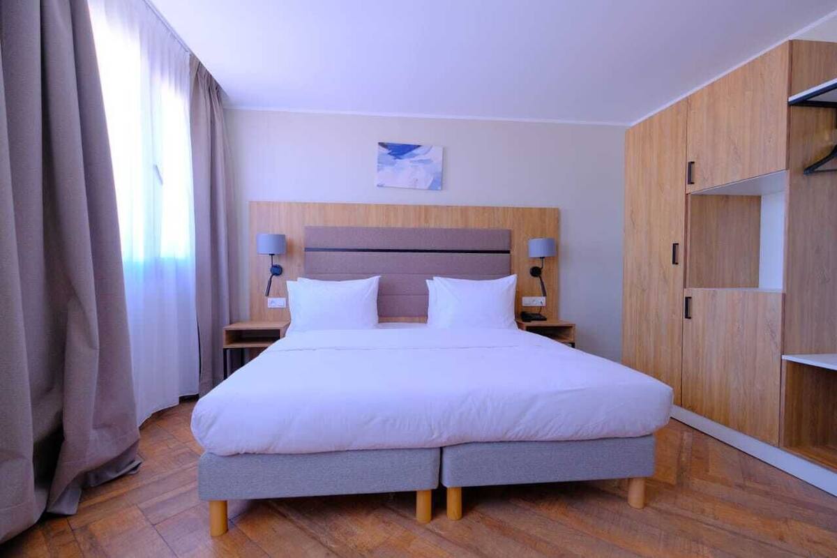 A modern hotel room with a large bed, wooden wardrobe, and a painting on the wall.