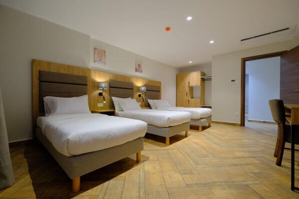 Une chambre d’hôtel avec deux lits simples, une tête de lit en bois, des lampes de chevet, un plancher en bois et un bureau en bois avec une chaise.