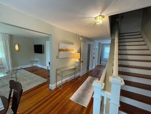 A spacious living area with hardwood floors, a staircase, and a flat-screen TV mounted on the wall.