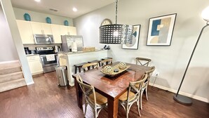 A modern kitchen with stainless steel appliances, a dining area with a wooden table and wicker chairs, and a hanging light fixture. - Comfy Villa 3BR Near Disney & Parks (Kissimmee)