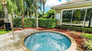 A hot tub surrounded by a landscaped garden with palm trees and a building in the background. - Comfy Villa 3BR Near Disney & Parks (Kissimmee)