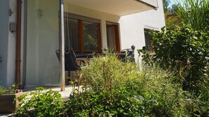 Uma casa de dois andares com varanda coberta, chaminé aparente e um jardim frontal.