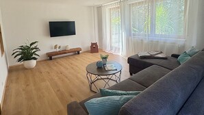 Uma sala de estar espaçosa com um sofá grande, uma mesa de centro e uma TV de tela plana na parede.