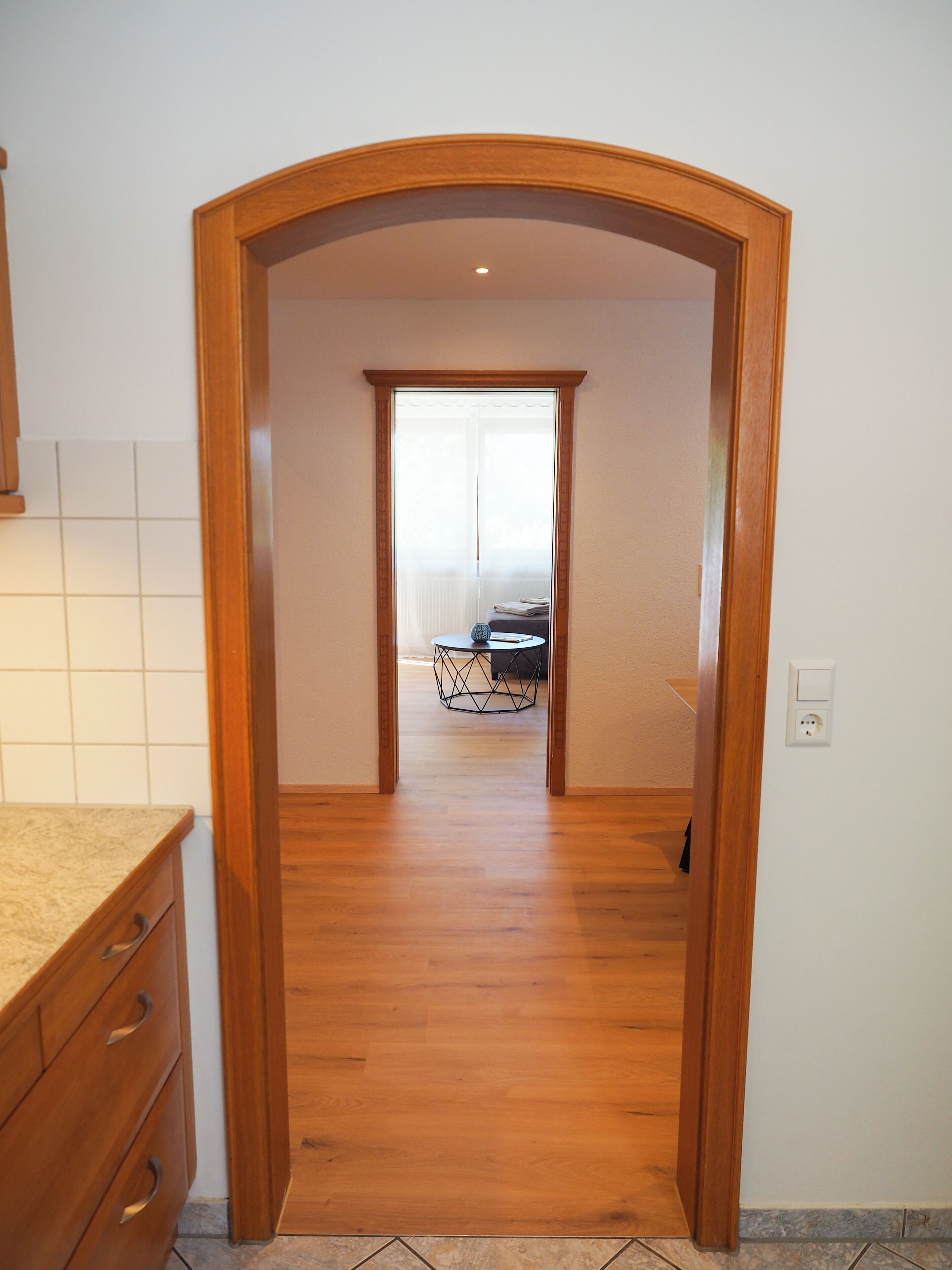 Un couloir avec une porte en bois qui donne sur une pièce où se trouvent une table ronde et une chaise.