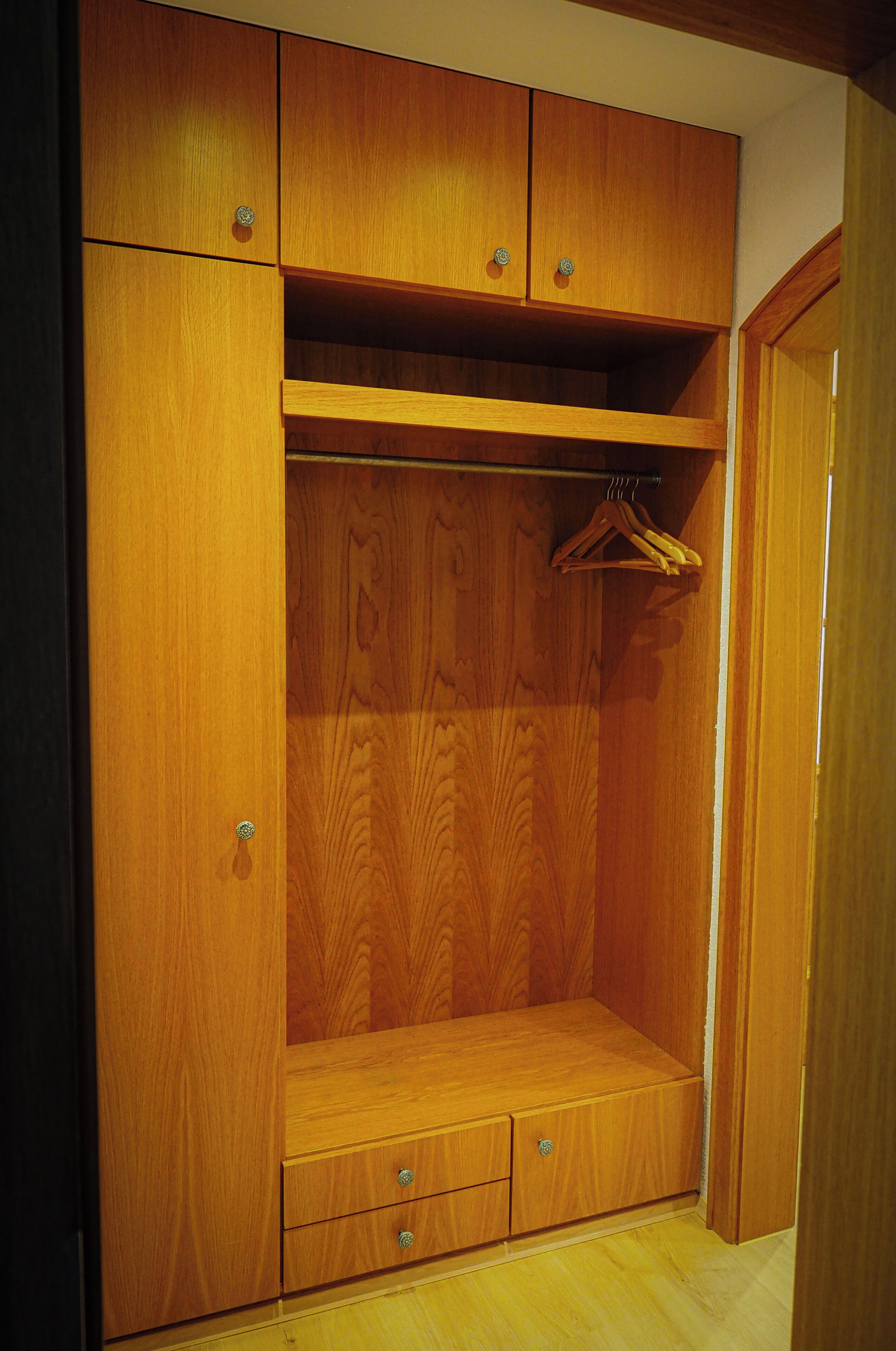 Ein hölzerner Kleiderschrank mit mehreren Fächern, darunter ein Kleiderbügelbereich und eine Schubladenebene.