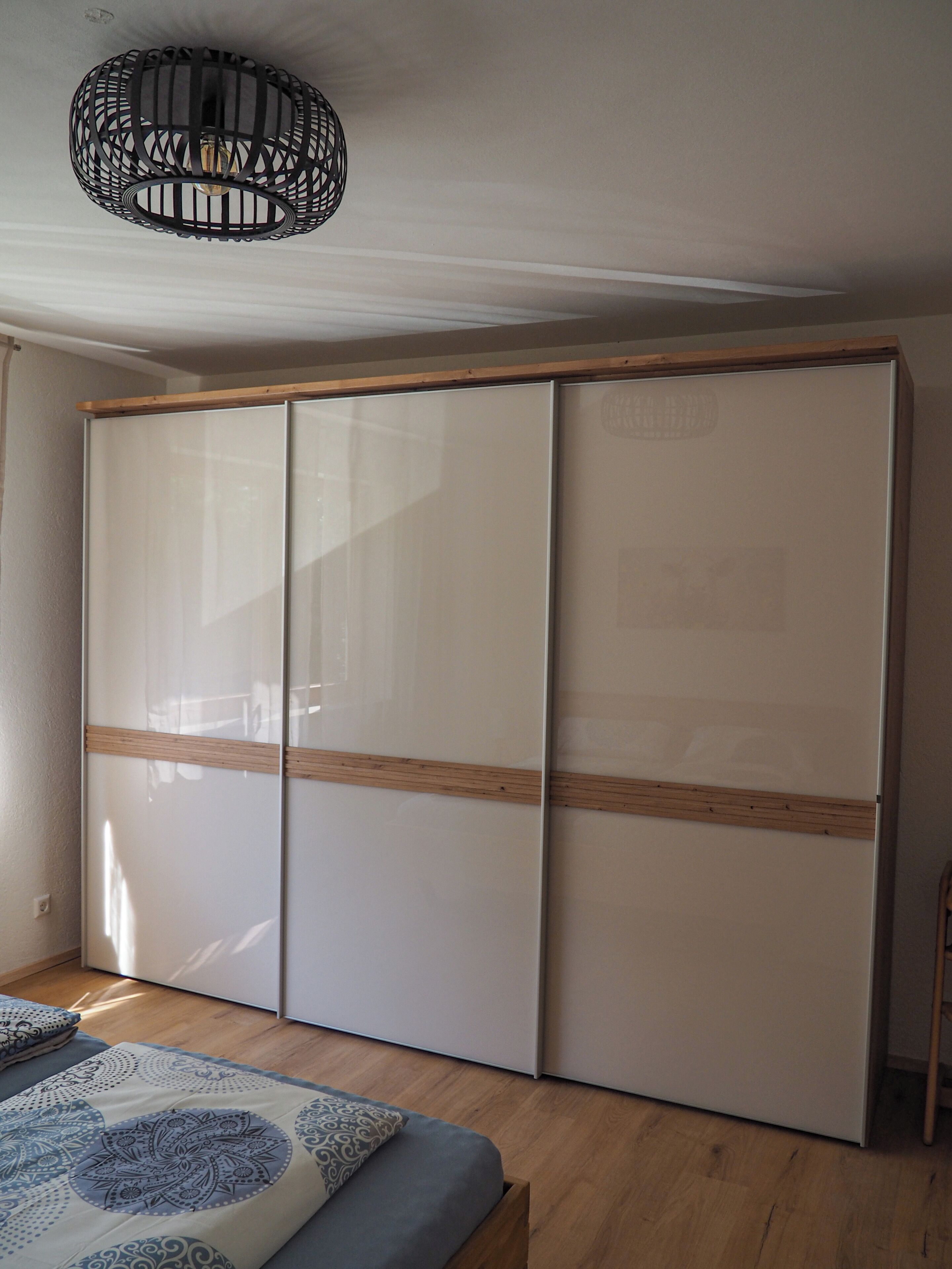 A room with a sliding wardrobe, a bed with patterned bedding, and a hanging light fixture.