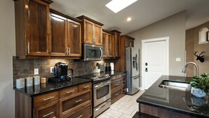 A modern kitchen with wooden cabinets, stainless steel appliances, and a large island with a sink. - Modern Comfort, cozy family home for work & leisure in the luxurious Southside (Lethbridge)