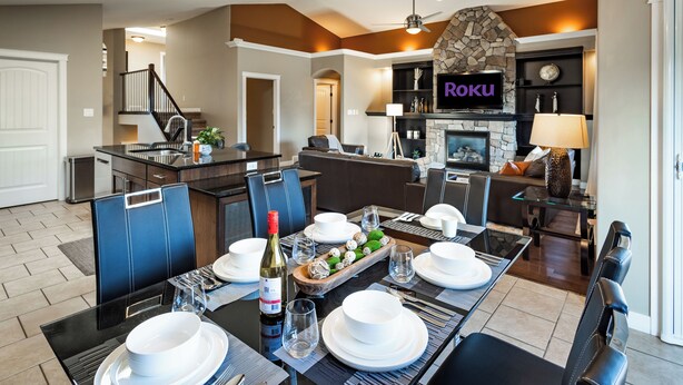 A modern kitchen with a dining area, a stone fireplace, and a TV displaying "Roku". - Modern Comfort, cozy family home for work & leisure in the luxurious Southside (Lethbridge)