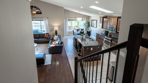 A spacious living area with a dark wood floor, a black leather sofa, and a dining area with a kitchen in the background. - Modern Comfort, cozy family home for work & leisure in the luxurious Southside (Lethbridge)