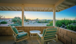 Une terrasse couverte avec deux chaises et une petite table, donnant sur un quartier résidentiel avec des maisons et un ciel dégagé.