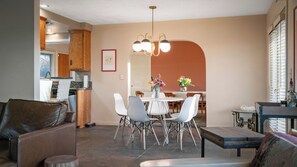 Un salon moderne avec un coin repas, une cuisine à l’arrière-plan et une grande fenêtre équipée de stores.