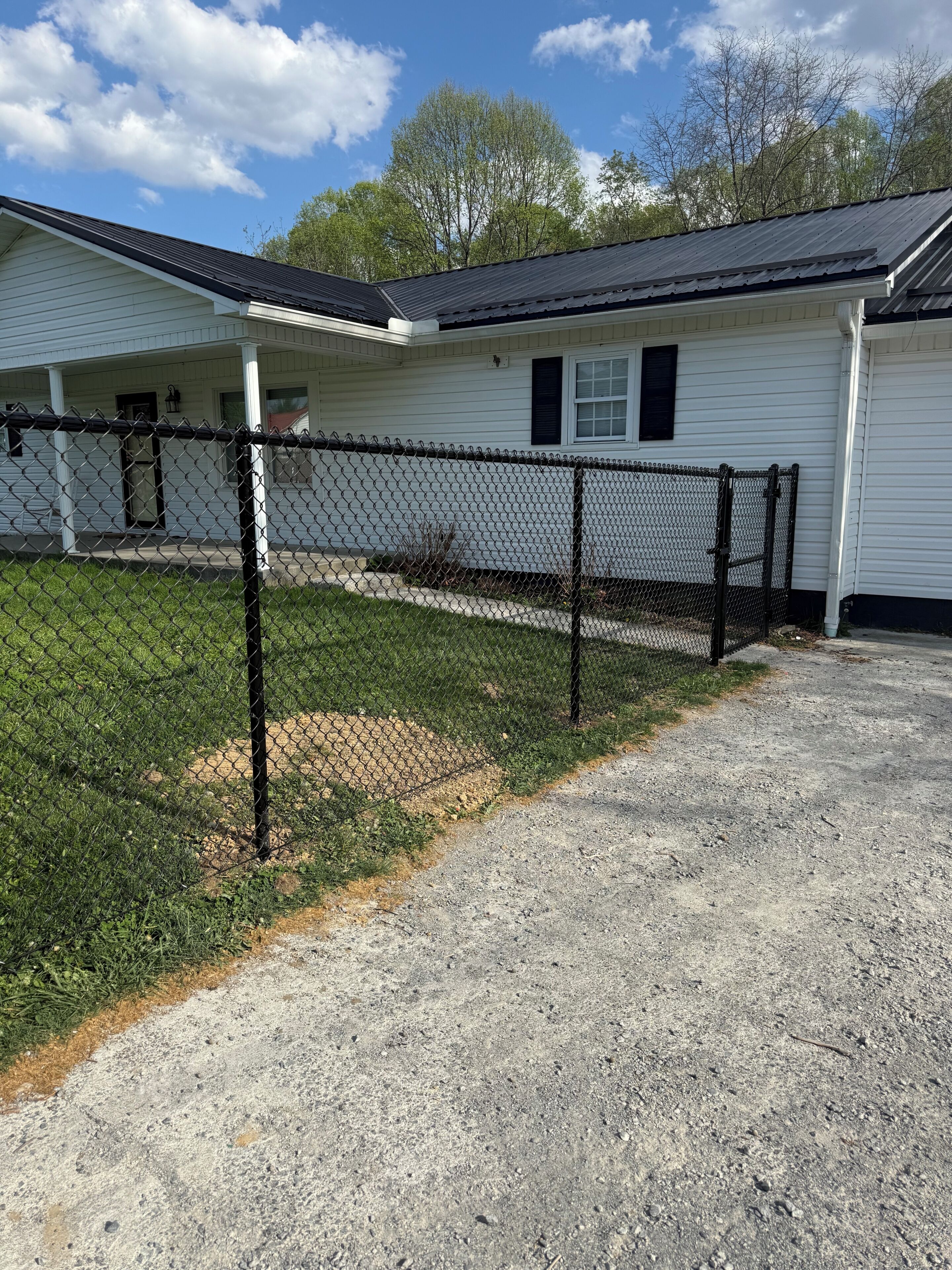 A single-story building with a chain-link fence, a gravel driveway, and a grassy area.