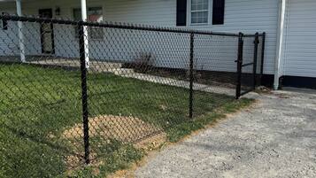 A single-story building with a chain-link fence, a gravel driveway, and a grassy area.