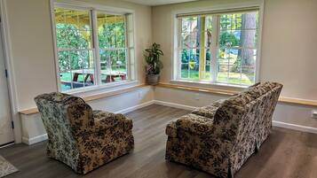 Ein geräumiges Zimmer mit zwei floralen Sofas, großen Fenstern mit Blick ins Freie und Holzboden.