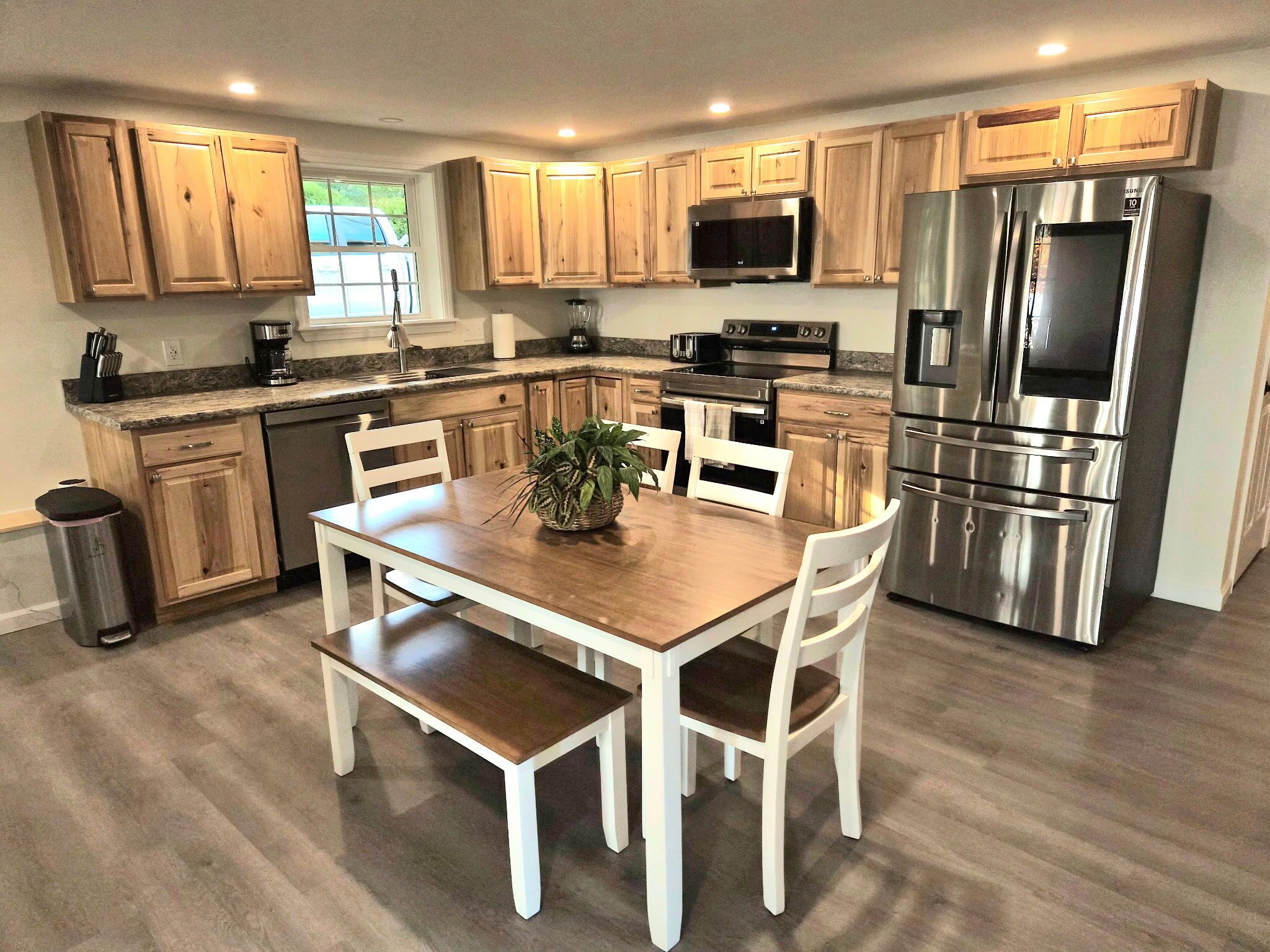 A modern kitchen with wooden cabinets, stainless steel appliances, and a dining area with white chairs and a wooden table.