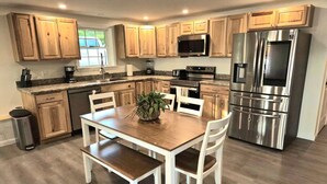 Une cuisine moderne avec des meubles en bois, des appareils en acier inoxydable et un coin repas comprenant des chaises blanches et une table en bois.
